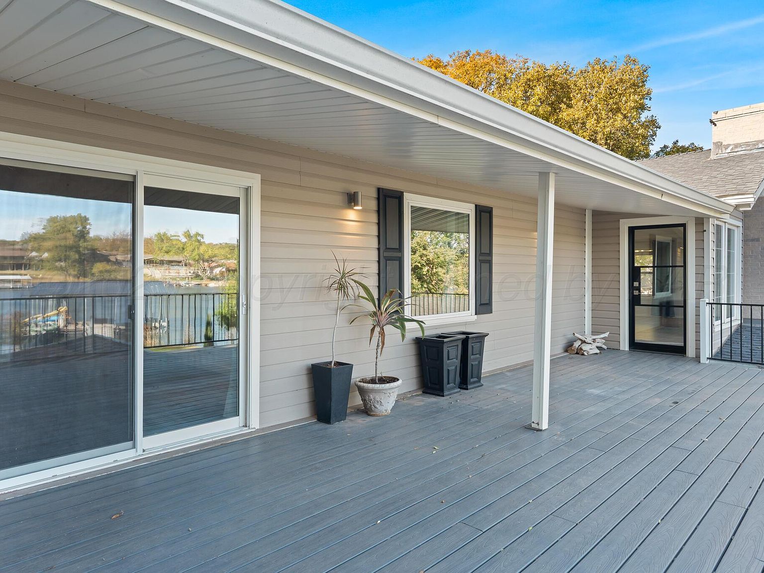 Long covered porch running the back of the house at 147 S Shore Dr, with sliding glass doors to the living rooms and a glimpse of the lake at the far left.
